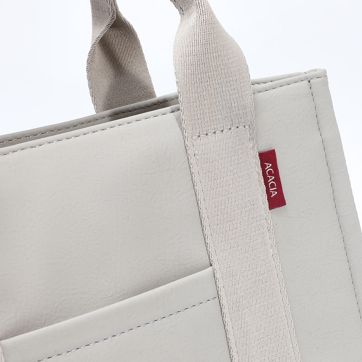 Close-up of ACACIA Fern Mini Tote strap and tag. Premium PU leather feel, water-repellent texture, strong stitching, and minimalist burgundy textile logo tag. Urban structured mini tote for everyday use.