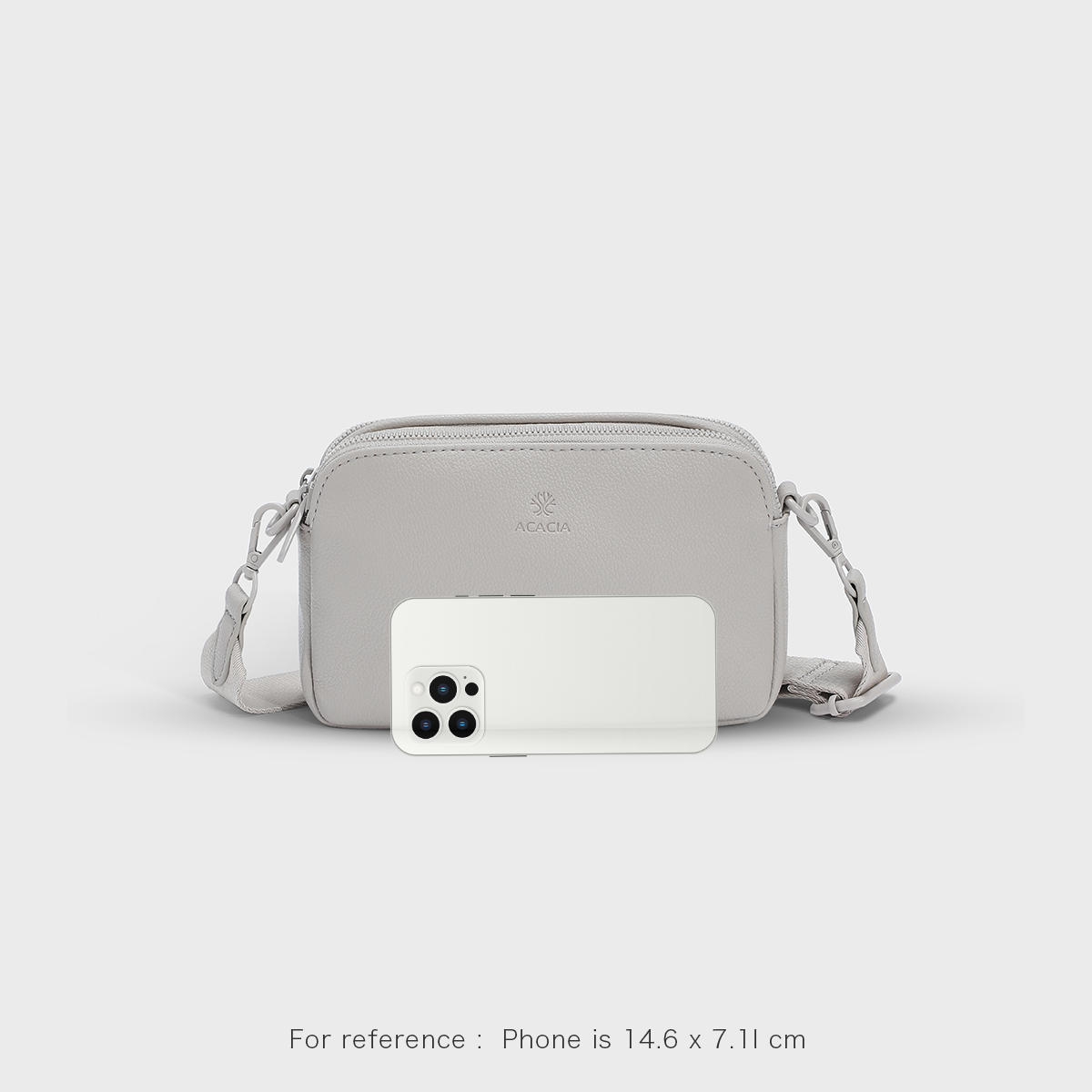 See the ACACIA Moss crossbody bag size next to a smartphone. Compact vegan leather sling with wide strap, double zippers, and unisex design. Perfect for commuting, travel, and everyday essentials.