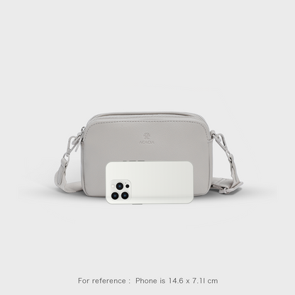 See the ACACIA Moss crossbody bag size next to a smartphone. Compact vegan leather sling with wide strap, double zippers, and unisex design. Perfect for commuting, travel, and everyday essentials.