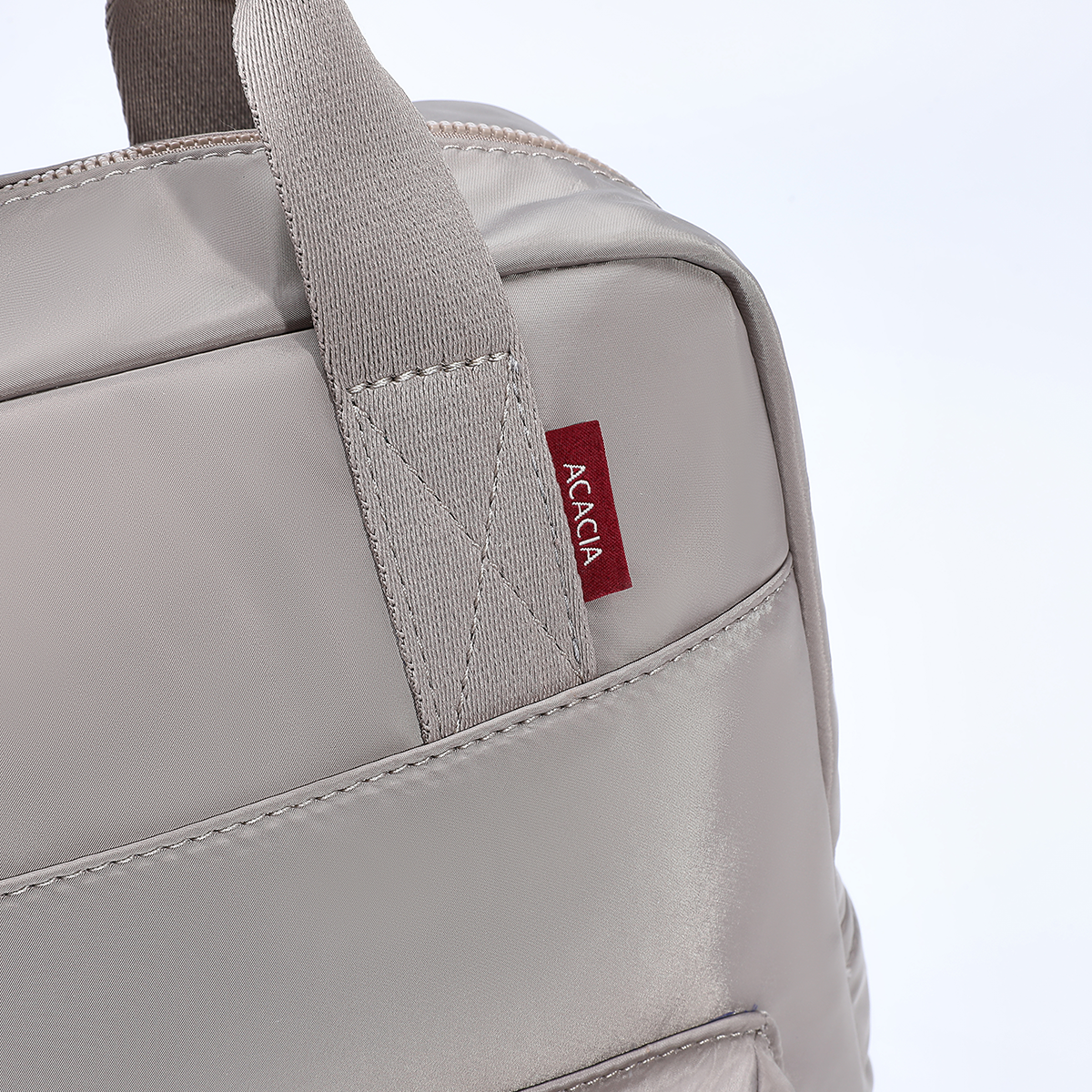 Close-up detail of the Reed Backpack showing reinforced top handles, premium stitching, metal hardware, and the signature ACACIA label. A stylish unisex backpack designed for durability and everyday use.